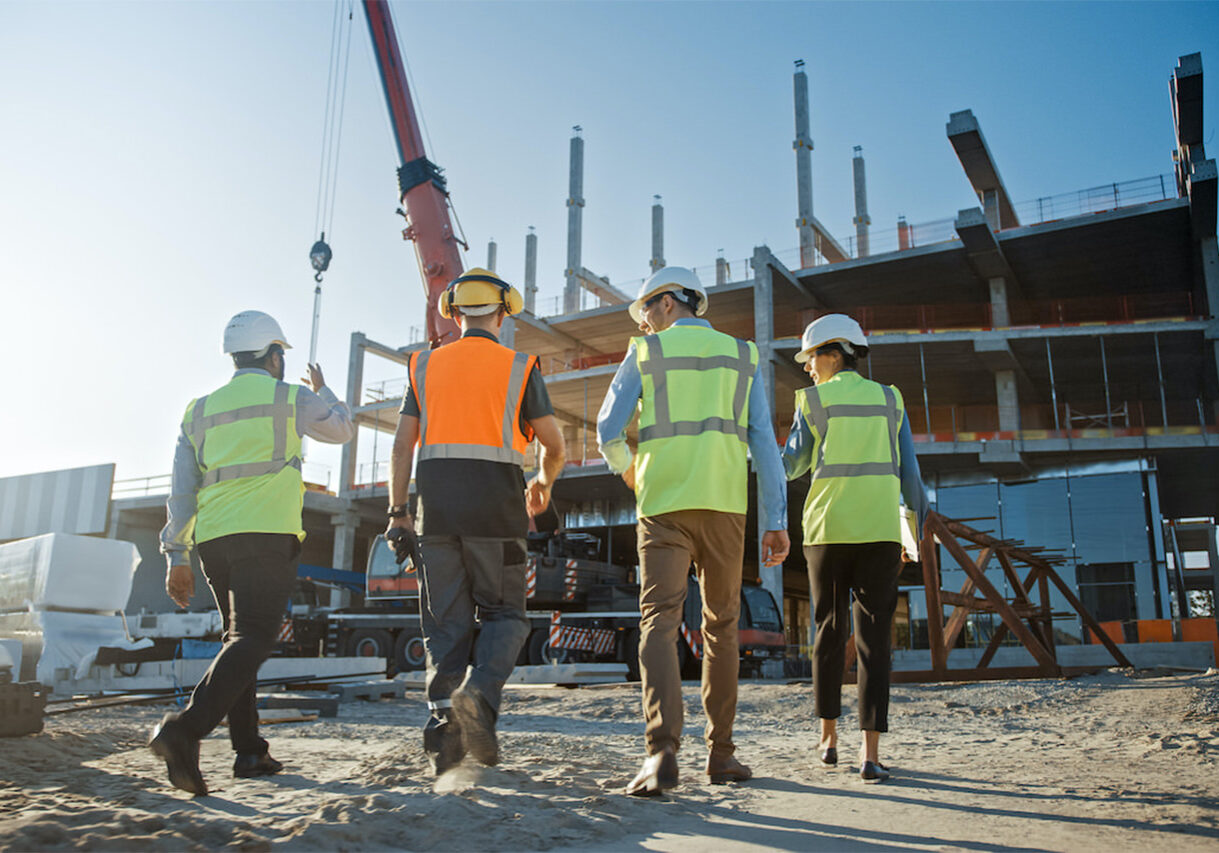 Diverse Team of Specialists Inspect Commercial, Industrial Building Construction Site. Real Estate Project with Civil Engineer, Investor and Worker. In the Background Crane, Skyscraper Formwork Frames
