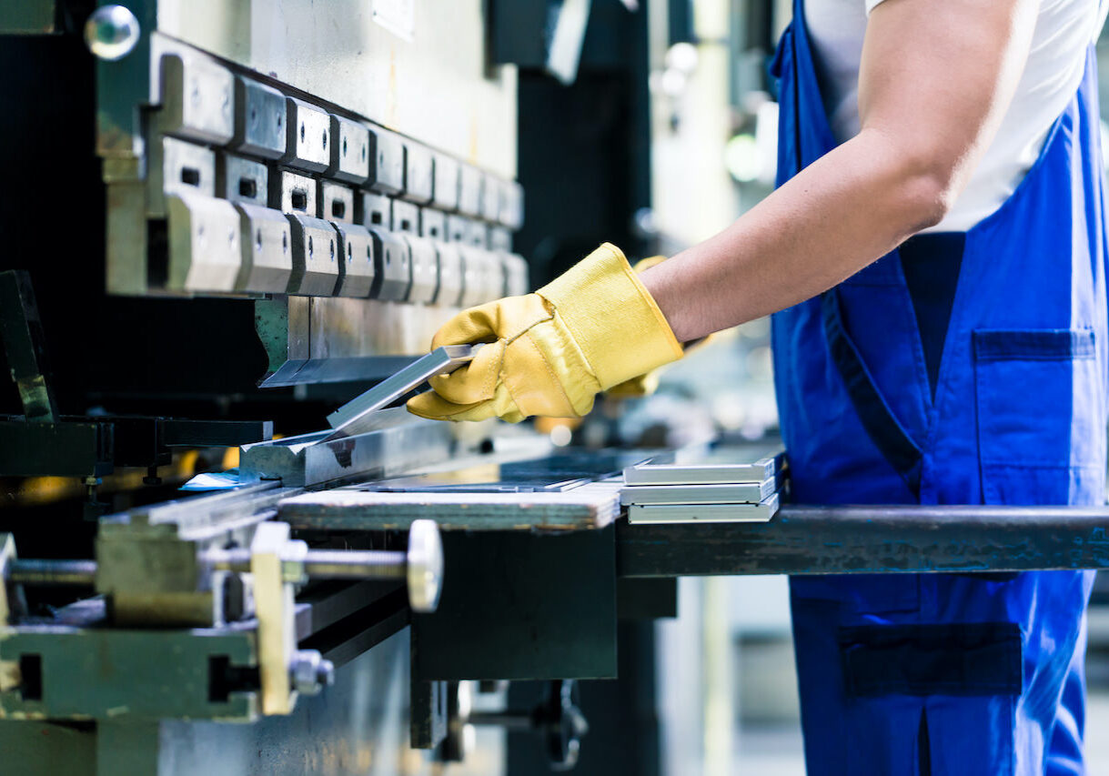 Asian worker in factory at metal skip machine putting work piece in