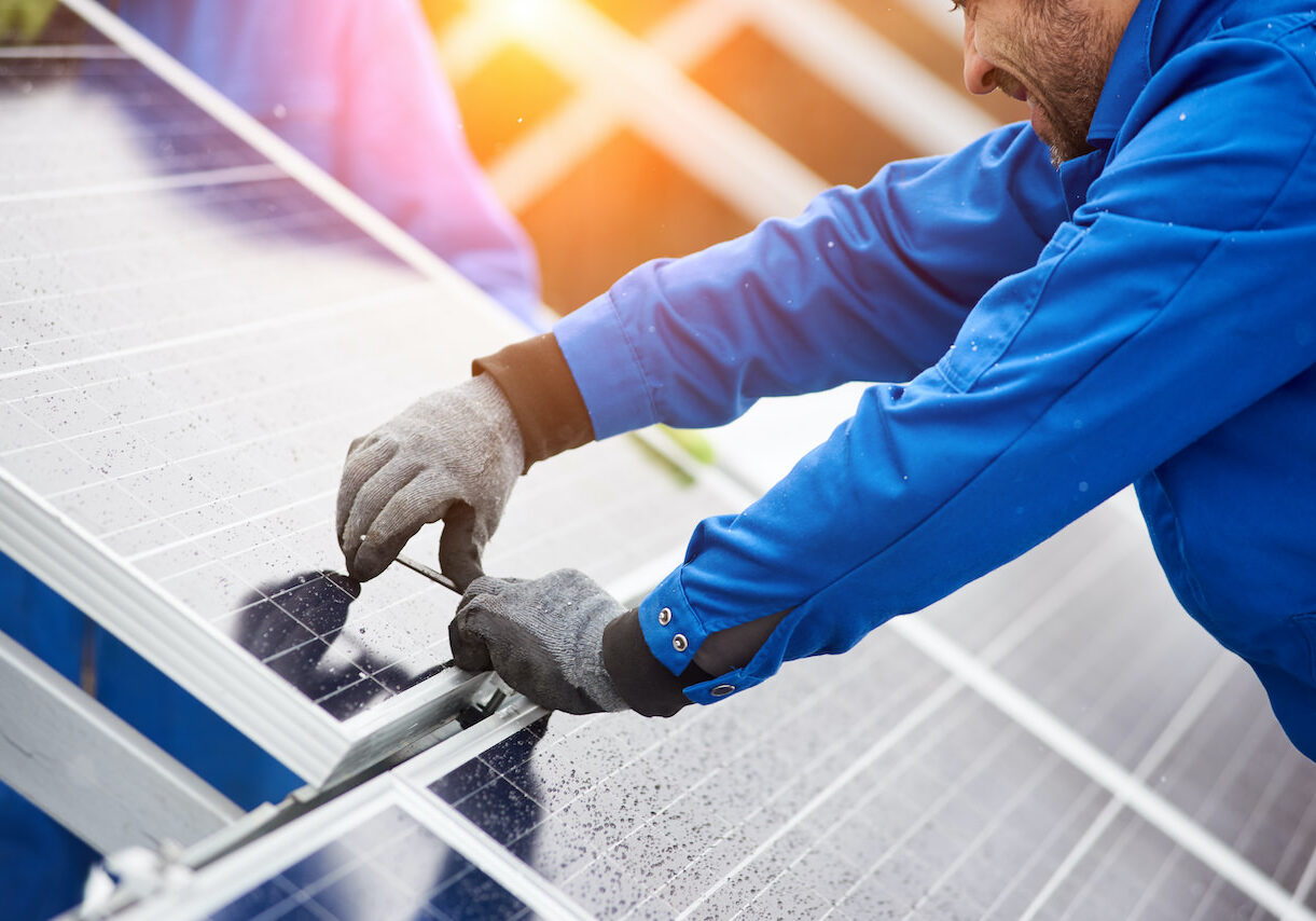 Smiling male technician in blue suit installing photovoltaic blue solar modules with screw. Man electrician panel sun sustainable resources renewable energy source alternative innovation